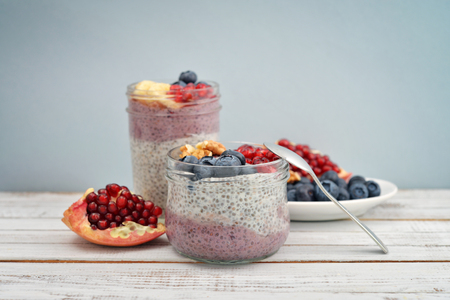 Pudding with chia seeds, yogurt and fresh fruits in glass jars on blue backgroundの写真素材