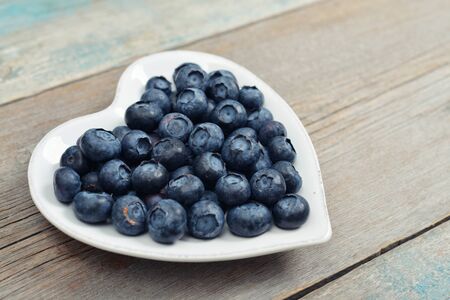 Plate in shape of heart with blueberries on wooden backgroundの写真素材