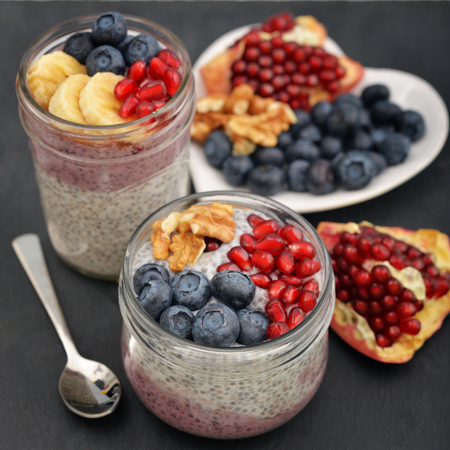 Pudding with chia seeds, yogurt and fresh fruits in glass jars on black backgroundの写真素材