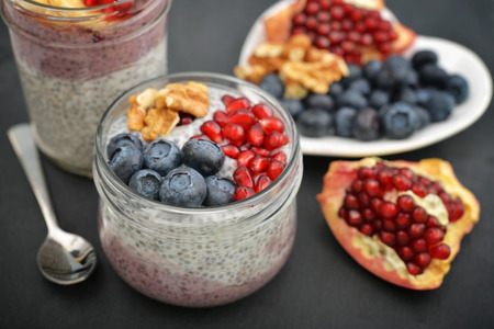 Pudding with chia seeds, yogurt and fresh fruits in glass jars on black backgroundの写真素材