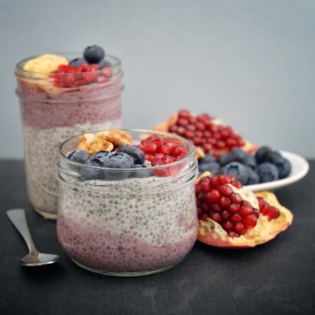 Pudding with chia seeds, yogurt and fresh fruits in glass jars on black backgroundの写真素材
