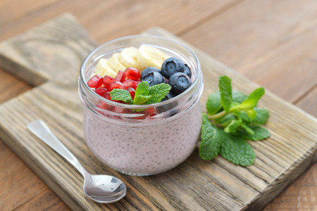 Pudding with chia seeds, yogurt and fresh fruits in glass jars on wooden backgroundの写真素材