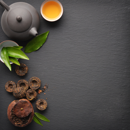 Teapot with cup and dry green tea pu-erh on black slate background, top viewの写真素材