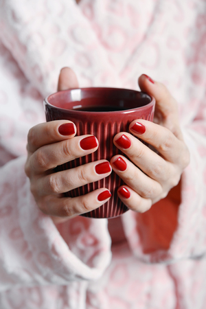 Women in pink bathrobe holds mug with coffee in handsの写真素材