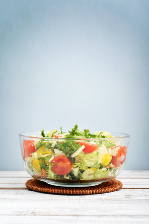 Salad mix with lettuce, cherry tomato, paprika and parmesan in glass bowl on blue backgroundの写真素材
