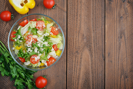 Salad mix with lettuce, cherry tomato, paprika and parmesan in glass bowl on wooden backgroundの写真素材