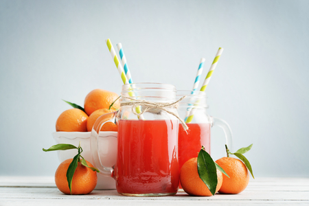 Citrus juice in jar with handle and fresh mandarin orange on blue backgroundの写真素材