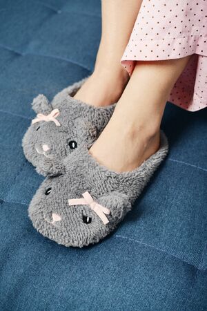 Female legs in cute slippers on the background of the blue couchの写真素材