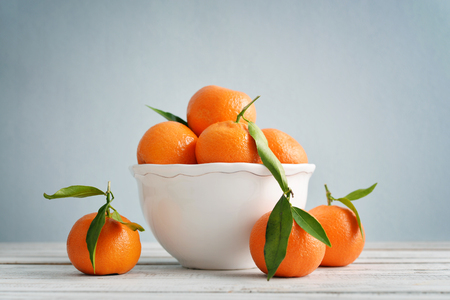 Tangerines with leaves in white bowl on blue backgroundの写真素材