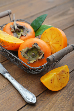 Ripe sweet persimmons in basket on wooden table closeupの写真素材