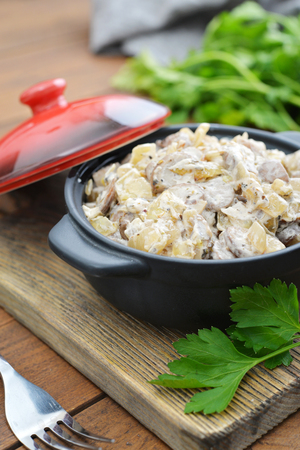 Fried mushrooms with sour cream in ceramic casserole on wooden backgroundの写真素材