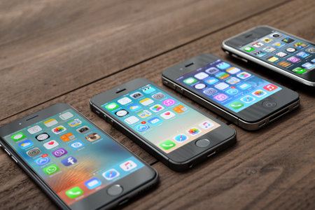 Kiev, Ukraine - March 05, 2016: Front view of a space grey color iPhones 6, 5s, 4 and 3gs generation showing the home screens on wooden background.のeditorial素材