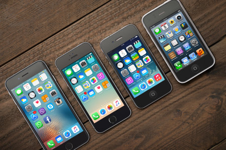 Kiev, Ukraine - March 05, 2016: Front view of a space grey color iPhones 6, 5s, 4 and 3gs generation showing the home screens on wooden background.のeditorial素材