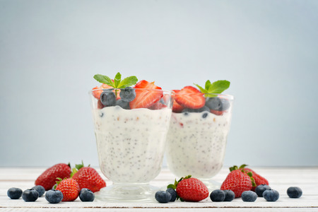 Pudding with chia seeds, yogurt and fresh fruits in glass on blue backgroundの写真素材