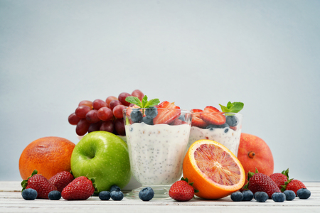 Pudding with chia seeds, yogurt and fresh fruits in glass on blue backgroundの写真素材