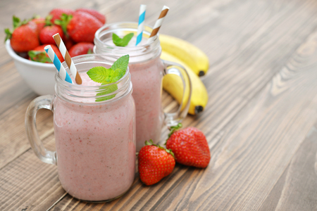 Fruit smoothies with strawberry, blueberry and banana in jar with handle on wooden background