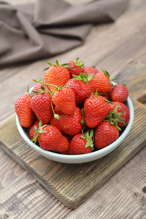 Fresh red strawberries in a ceramic bowl on wooden backgroundの写真素材