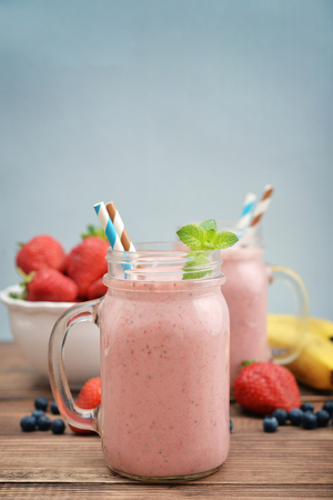 Fruit smoothies with strawberry, blueberry and banana in jar with handle on blue backgroundの写真素材