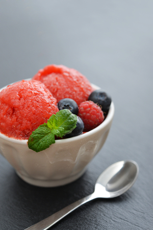 Fruit strawberry sorbet with raspberry, blueberry and mint in a bowl on black slate backgroundの写真素材