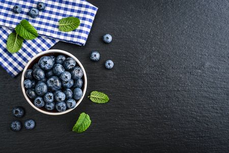 Fresh blueberry in bowl with wooden spoons and nupkin on black slate background, top viewの写真素材