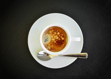 Espresso coffee in small white cup with a spoon on black slate background, top viewの写真素材