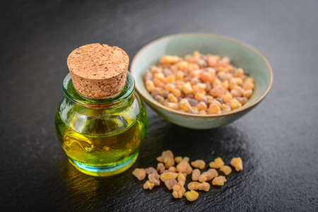 A bottle of frankincense essential oil with frankincense resin crystals on black slate backgroundの写真素材