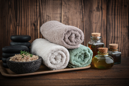 Towels with sea salt, massage oil in vintage bottle, candles and stones for stone massage on wooden backgroundの写真素材