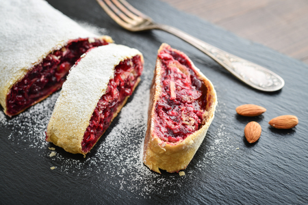 Cherry strudel with almond and powdered sugar on black slate backgroundの写真素材