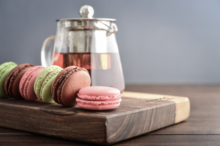 Different kinds of macaroons in row with teapot on wooden background closeupの写真素材