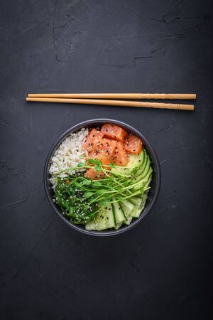 Hawaiian salmon poke bowl with seaweed, avocado, sesame seeds and cucumber on black background. Top view, flat layの写真素材