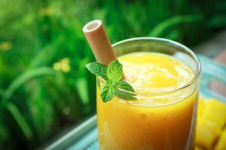 Mango smoothie in glass with bamboo drinking straws on wooden table outdoor, closeupの写真素材