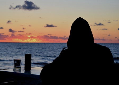 Silhouette of young man having drink near sea at sunset