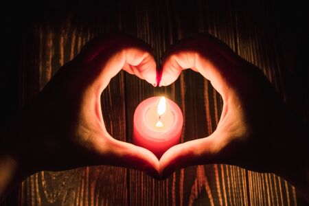 Heart-shaped female hands around burning red candleの写真素材