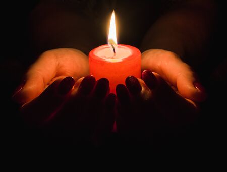Female hands holding a burning candle in the darkの写真素材