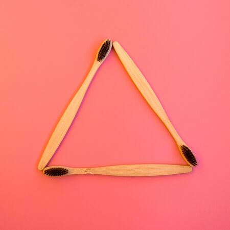 Recycling symbol made of bamboo toothbrushes on pink background