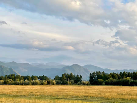 Beautiful dramatic sky over mountain ridges and yellow autumn field, Altai, Russia