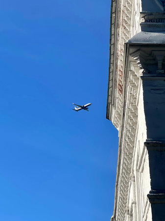 Airplane flying in the blue sky over the roofs of city buildings