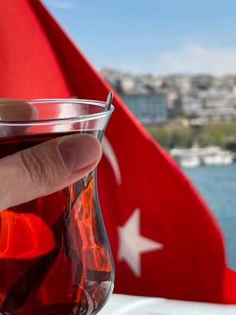 A cup of tea in a woman's hand against the background of the Turkish flag, Bosphorus and Istanbul, Turkeyの写真素材