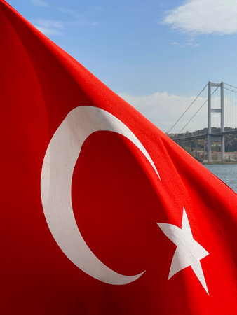 Turkish flag fluttering in the wind against Istanbul and the Golden Horn Bridge in the background,...