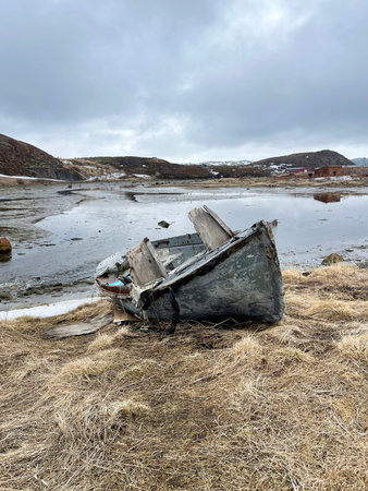 A weathered wooden boat decays on the shore Barents Sea. Gray sky, cold wind, yellow grass. Teriberka, Russiaの写真素材