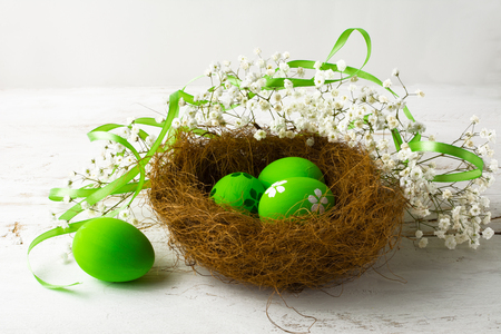 Green Easter eggs in a nest with green satin ribbon on a white wooden backgroundの写真素材