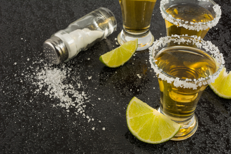 Gold tequila shot with lime on black background, close up. Tequila shot. Tequila. Gold Mexican tequilaの写真素材