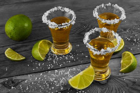 Three shots of gold tequila with lime and salt on the black background. Vintage toned photo. Tequila shot. Gold Mexican tequila. Tequilaの写真素材