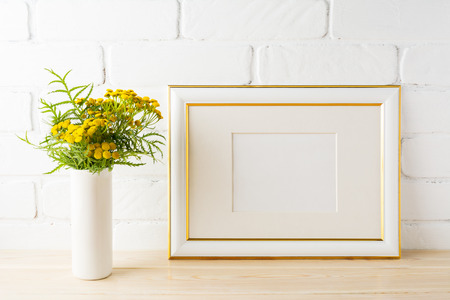 Gold decorated landscape frame mockup with wild deep rich yellow flowers in vase near painted brick walls. Empty frame mock up for presentation design.  Template framing for modern art.の写真素材