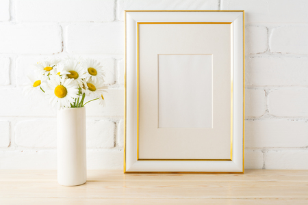 Gold decorated frame mockup with wild daisy flower in styled vase near painted brick wall. Empty frame mock up for presentation design.  Template framing for modern art. の写真素材