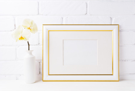 Gold decorated landscape frame mockup with soft yellow orchid in vase. Empty frame mock up for...
