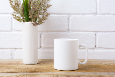 White coffee mug mockup with meadow grass and green leaves in cylinder vase near painted brick wall.  Empty mug mock up for design promotion.の写真素材