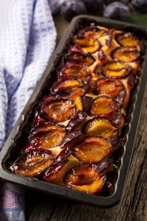 Rustic plum pie in the baking tray and napkin on the wooden backgroundの写真素材