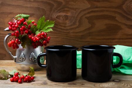 Two black campfire enamel coffee mug mockup with antique jug and cranberry branches.  Empty mug mock up for design promotion.の写真素材