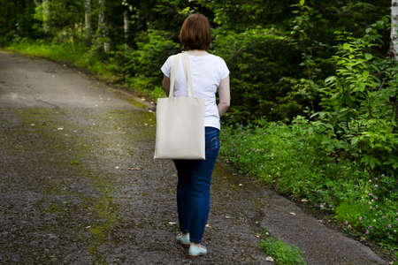Woman in white t-shirt carrying empty reusable shopping bag mockup. Female hand holding canvas eco...